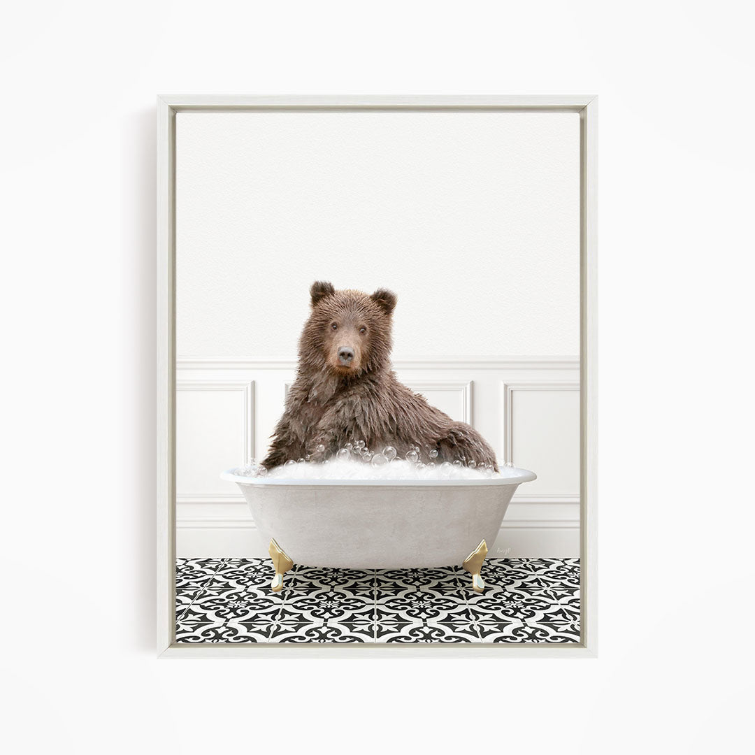 A brown bear sitting in a white bathtub filled with bubbles, looking directly at the camera.