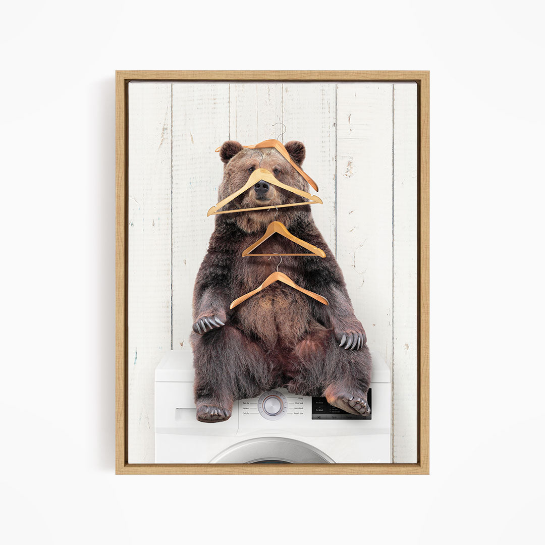 A brown bear sitting on top of a washing machine, surrounded by multiple wooden hangers.