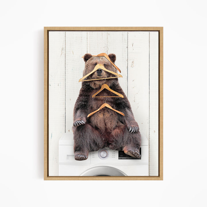 A brown bear sitting on top of a washing machine, surrounded by multiple wooden hangers.