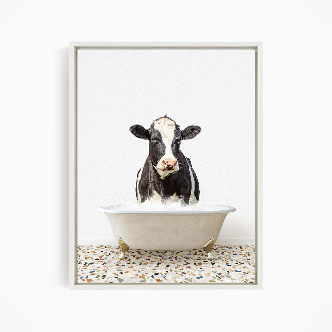 A black and white cow standing in a white bathtub filled with water, creating a whimsical and humorous scene.