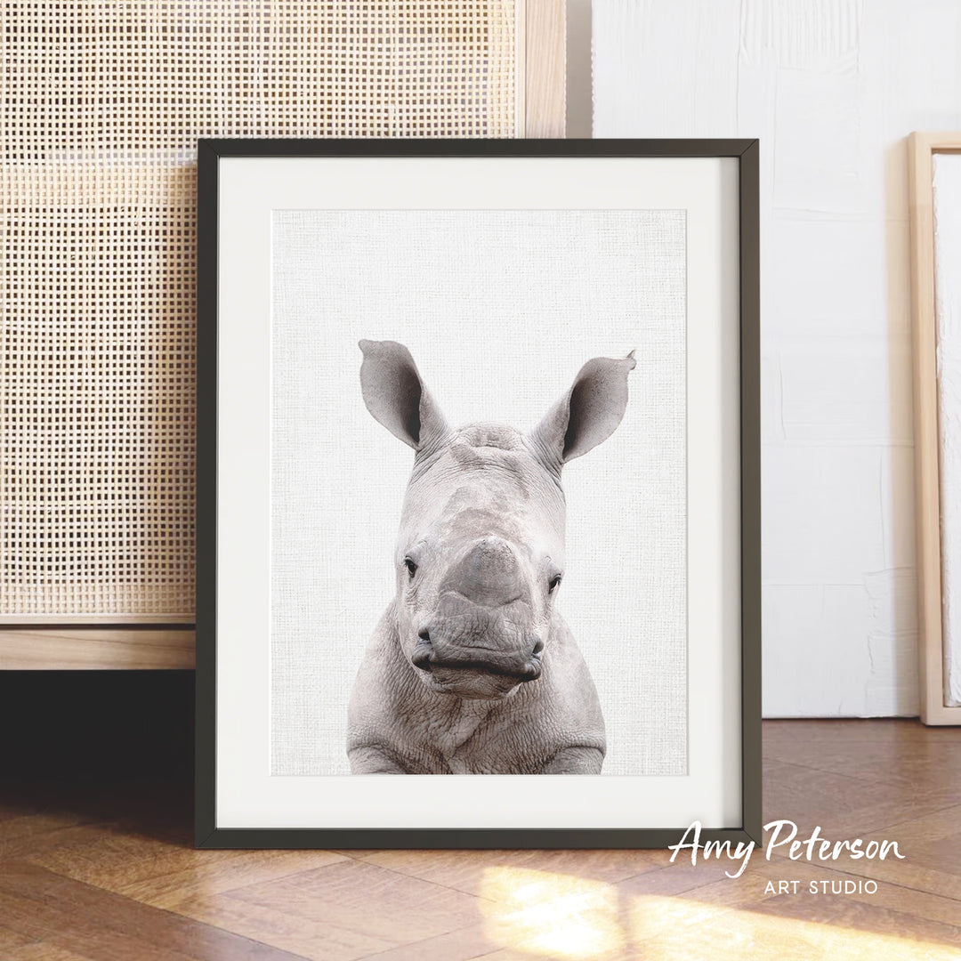 A framed photograph of a rhinoceros is displayed on a wooden floor, with a woven basket visible in the background.
