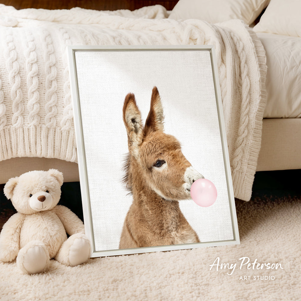A framed image of a donkey blowing a bubble gum bubble is displayed on a bed, accompanied by a teddy bear.