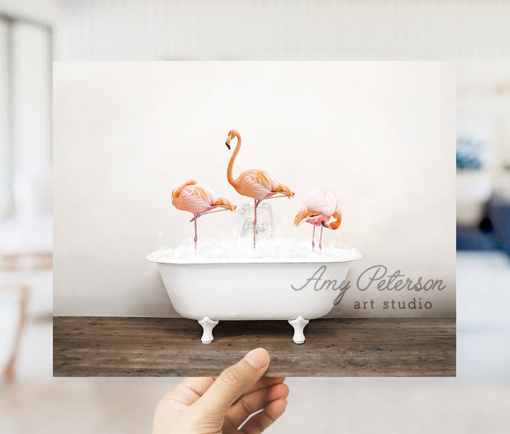 a person holding up a card with three flamingos in a bathtub