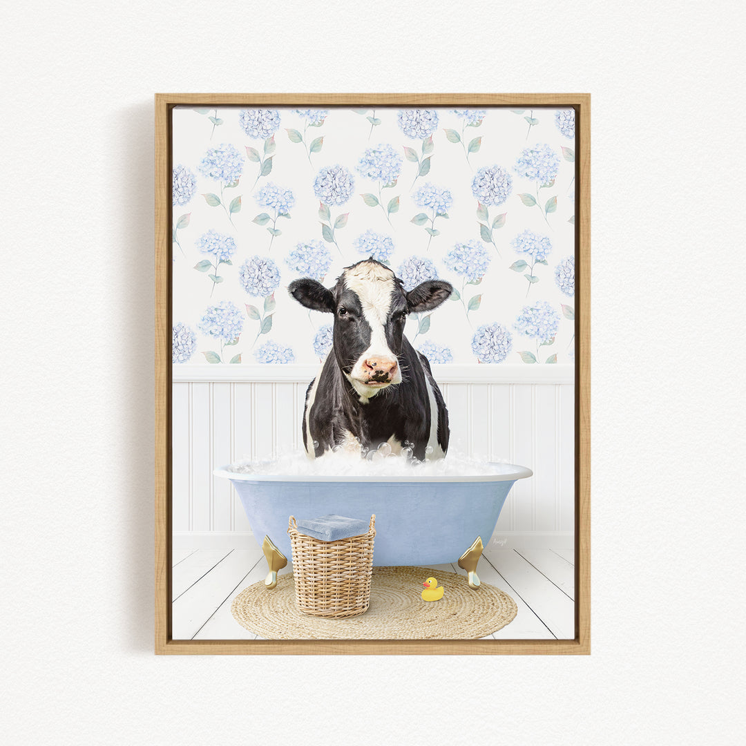 A black and white cow is sitting in a blue bathtub filled with water, surrounded by a wicker basket and two rubber duckies.