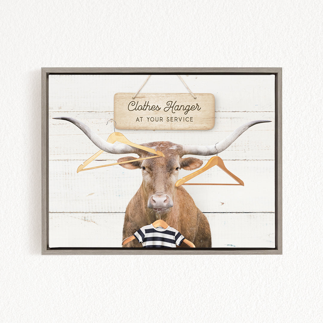 A bull with large horns is wearing a striped shirt and standing in front of a sign that says "Clothes Hanger at your service".