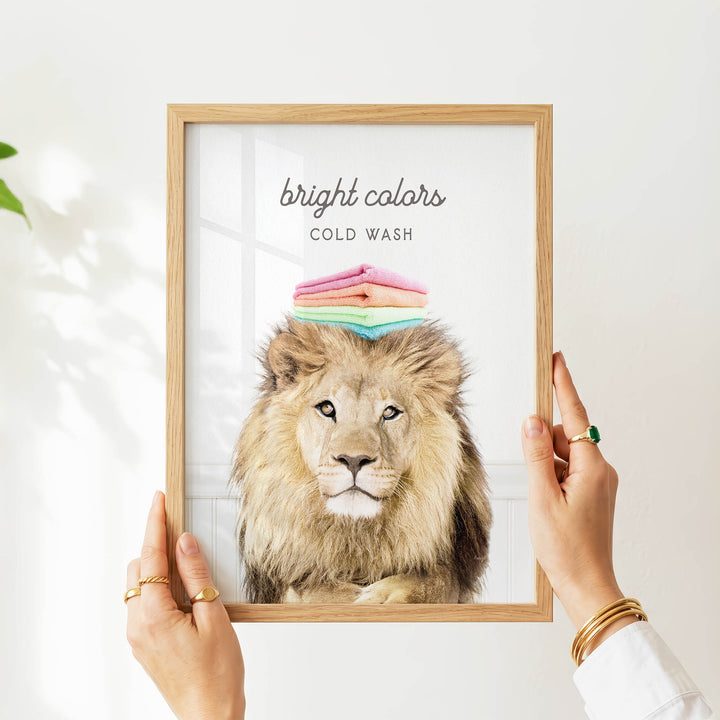 A person's hands are holding a framed picture of a lion with a stack of colorful towels on its head.