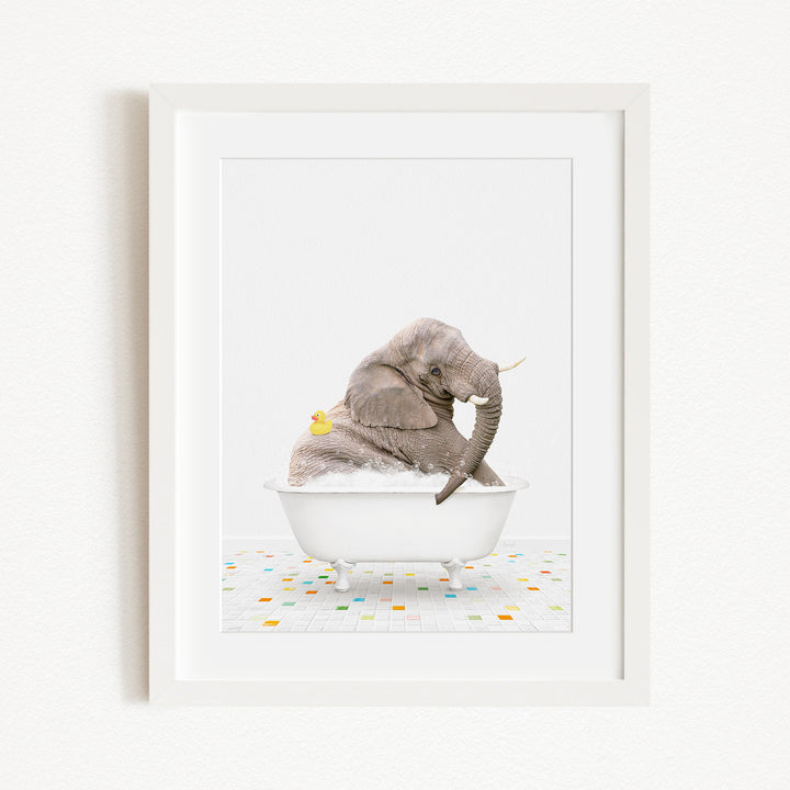 A gray elephant is sitting in a white bathtub filled with bubbles, with a yellow rubber duck floating next to it.
