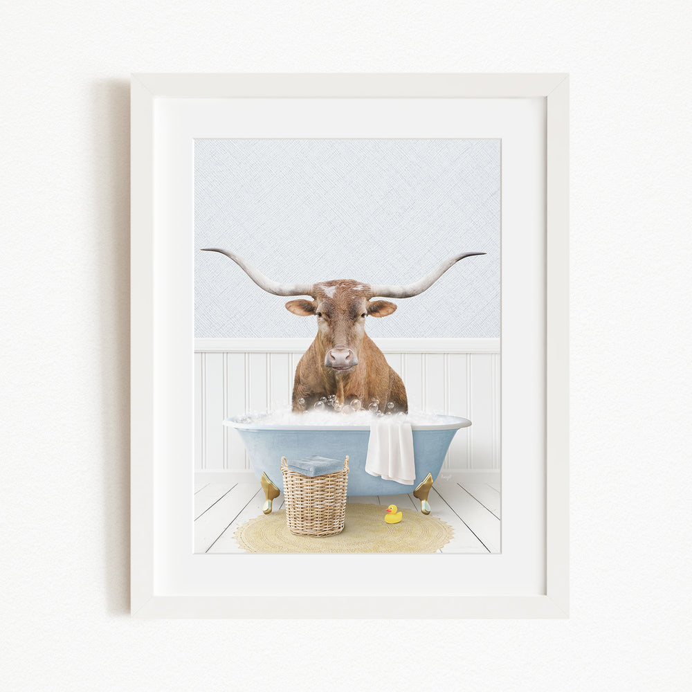A brown cow with large horns is sitting in a blue bathtub filled with water, surrounded by a yellow rubber duck and a basket.