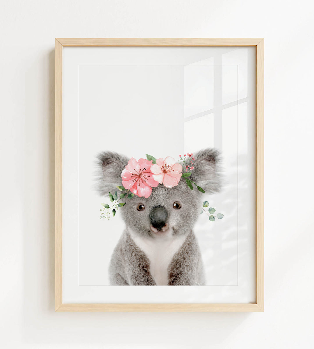 A framed image of a koala bear wearing a floral crown of pink flowers and greenery.