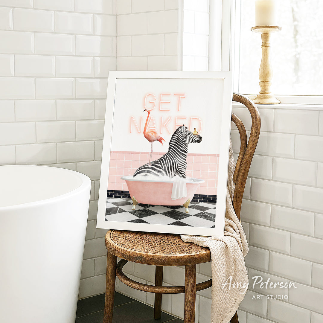 a framed artwork depicting a zebra sitting in a pink bathtub, with a flamingo standing nearby. The artwork is displayed on a wooden chair in a bathroom setting.