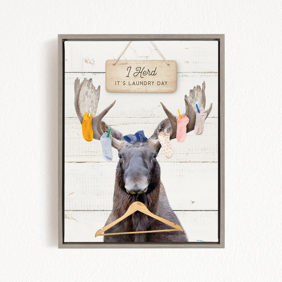 A framed image depicting a moose with a sign above it that says "I herd it's laundry day".
