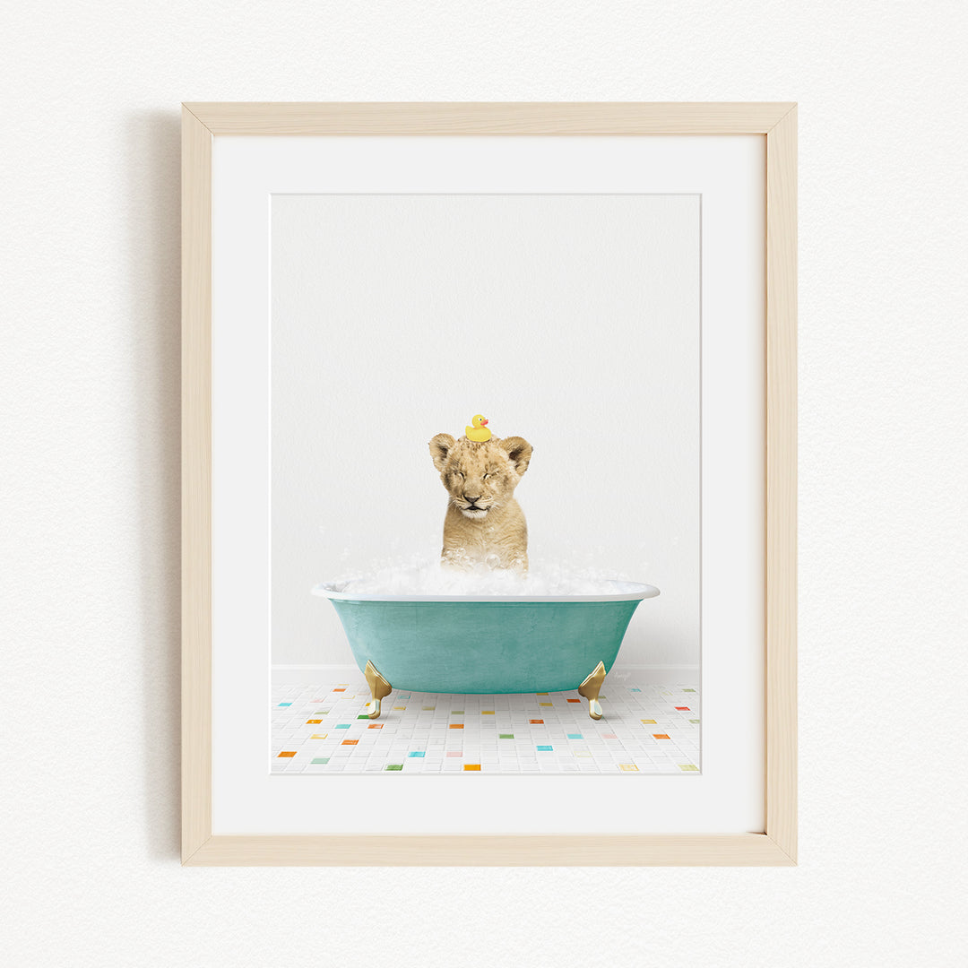 A young lion cub is sitting in a blue bathtub filled with bubbles, with a yellow rubber duck floating on the water.