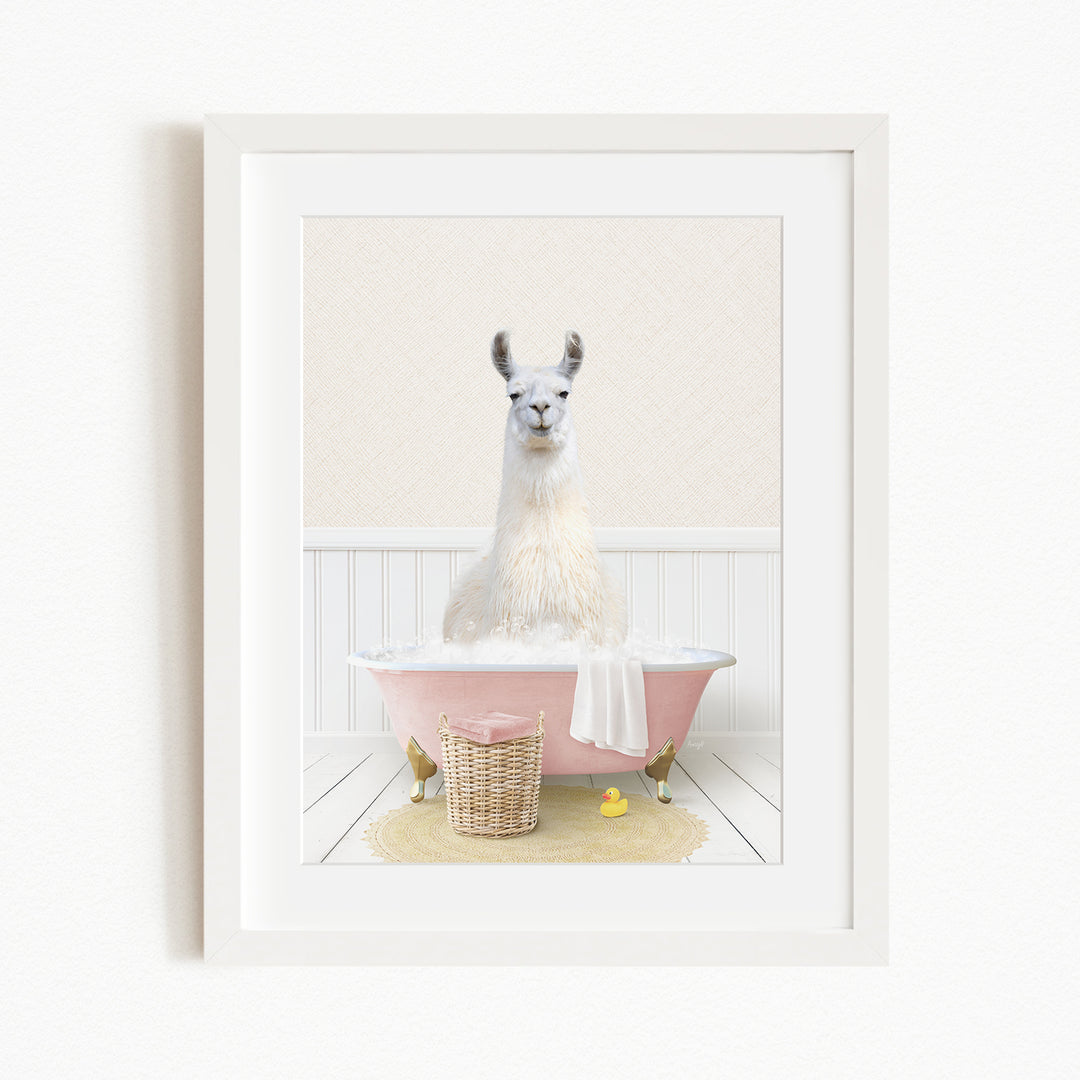 A white llama sitting in a pink bathtub filled with bubbles, surrounded by a yellow rubber duck and a basket.