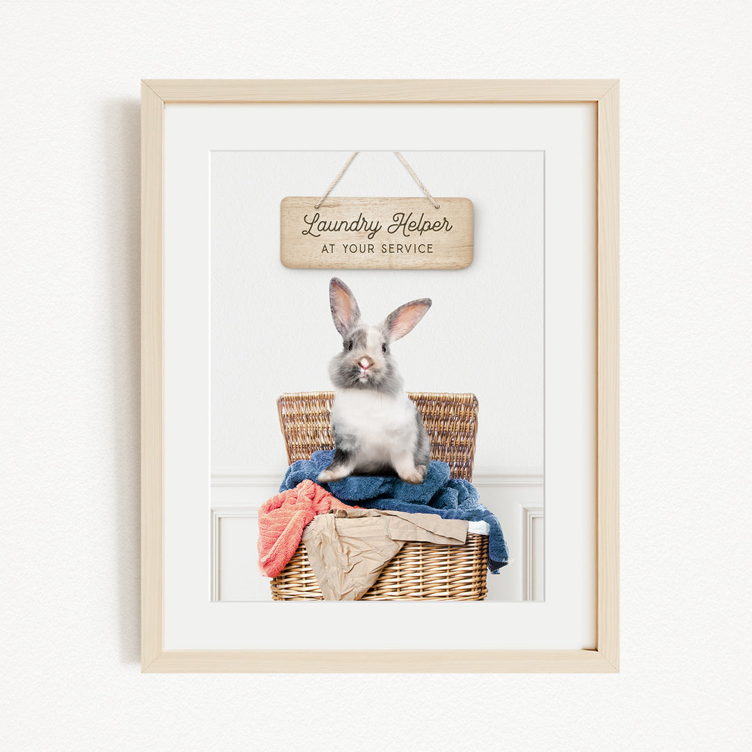 A framed image of a rabbit sitting in a wicker laundry basket, with a sign above that reads "Laundry Helper at your service".