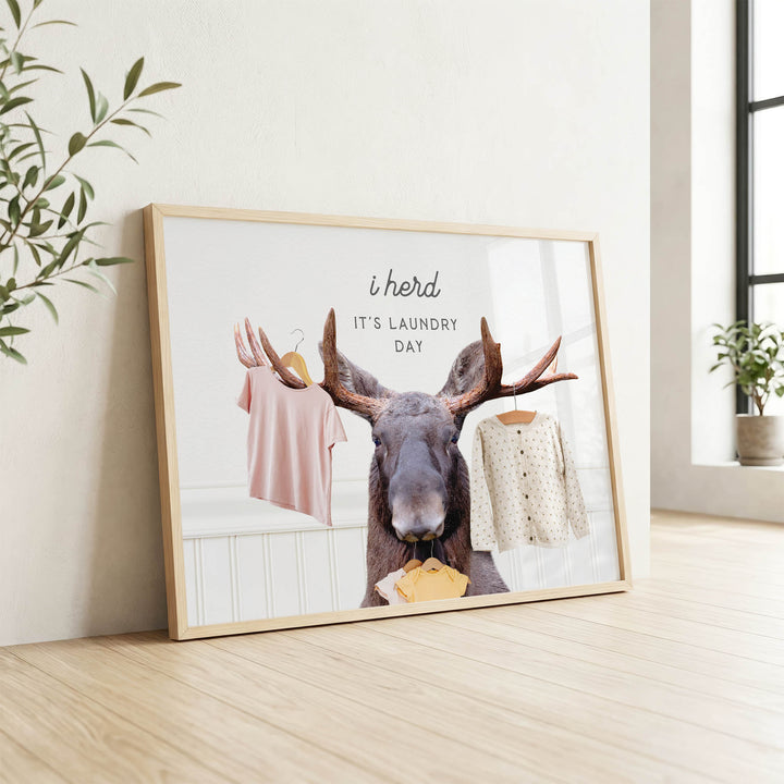 A framed poster with a moose holding clothes, accompanied by the text "It's laundry day"
