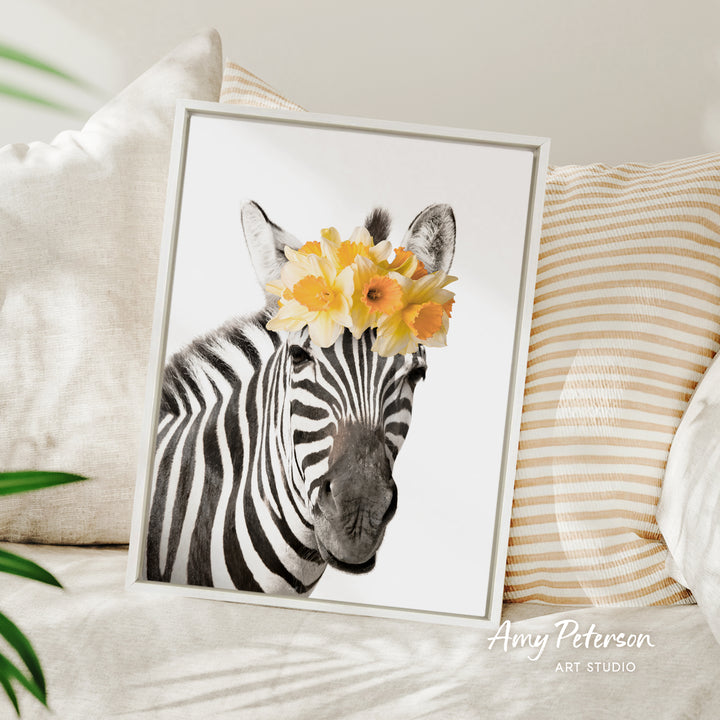 A framed photograph of a zebra wearing a yellow flower crown, placed on a couch with striped pillows.