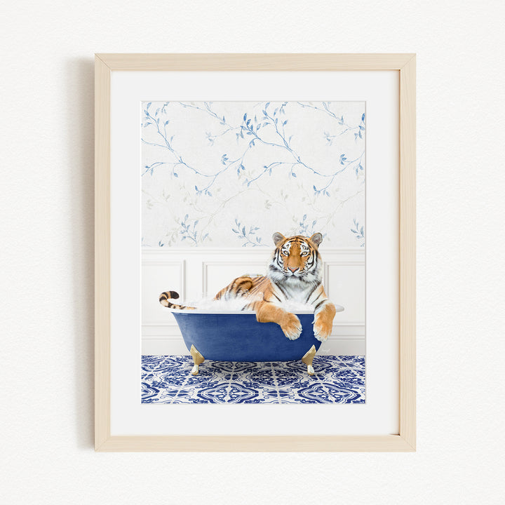 A tiger is sitting in a blue bathtub, surrounded by a patterned tile floor and a white wall with blue floral wallpaper.