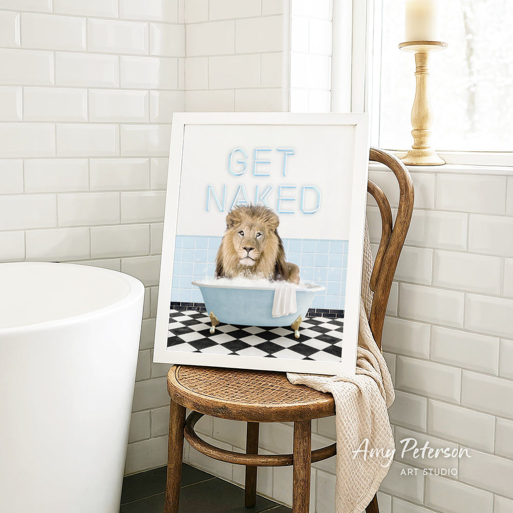 A framed image of a lion sitting in a bathtub with the text "GET NAKED" on it, placed on a wooden chair in a bathroom setting.