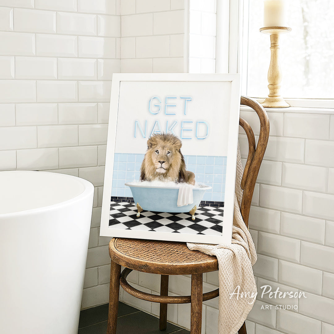 A framed image of a lion sitting in a bathtub with the text "GET NAKED" on it, placed on a wooden chair in a bathroom setting.