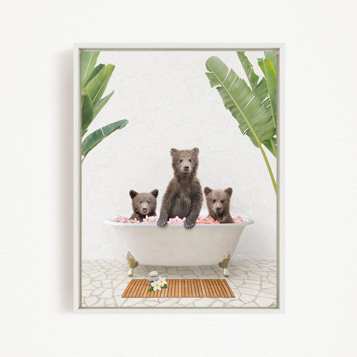 Three brown bears sitting in a white bathtub filled with pink flowers, surrounded by green leaves.