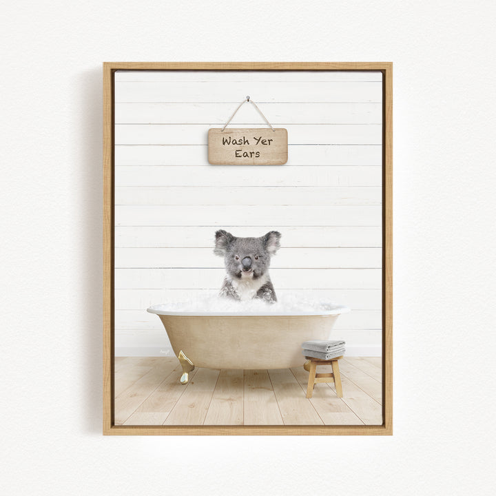 A koala sitting in a bathtub, with a wooden sign above that reads "Wash Your Ears".