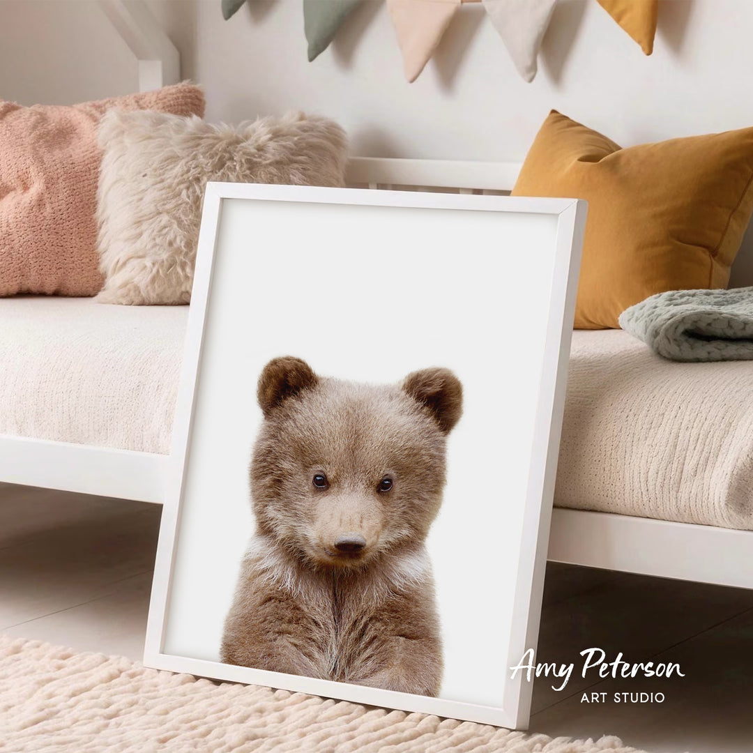A framed image of a cute brown bear is displayed in a cozy living room setting with a white bed and colorful pillows in the background.