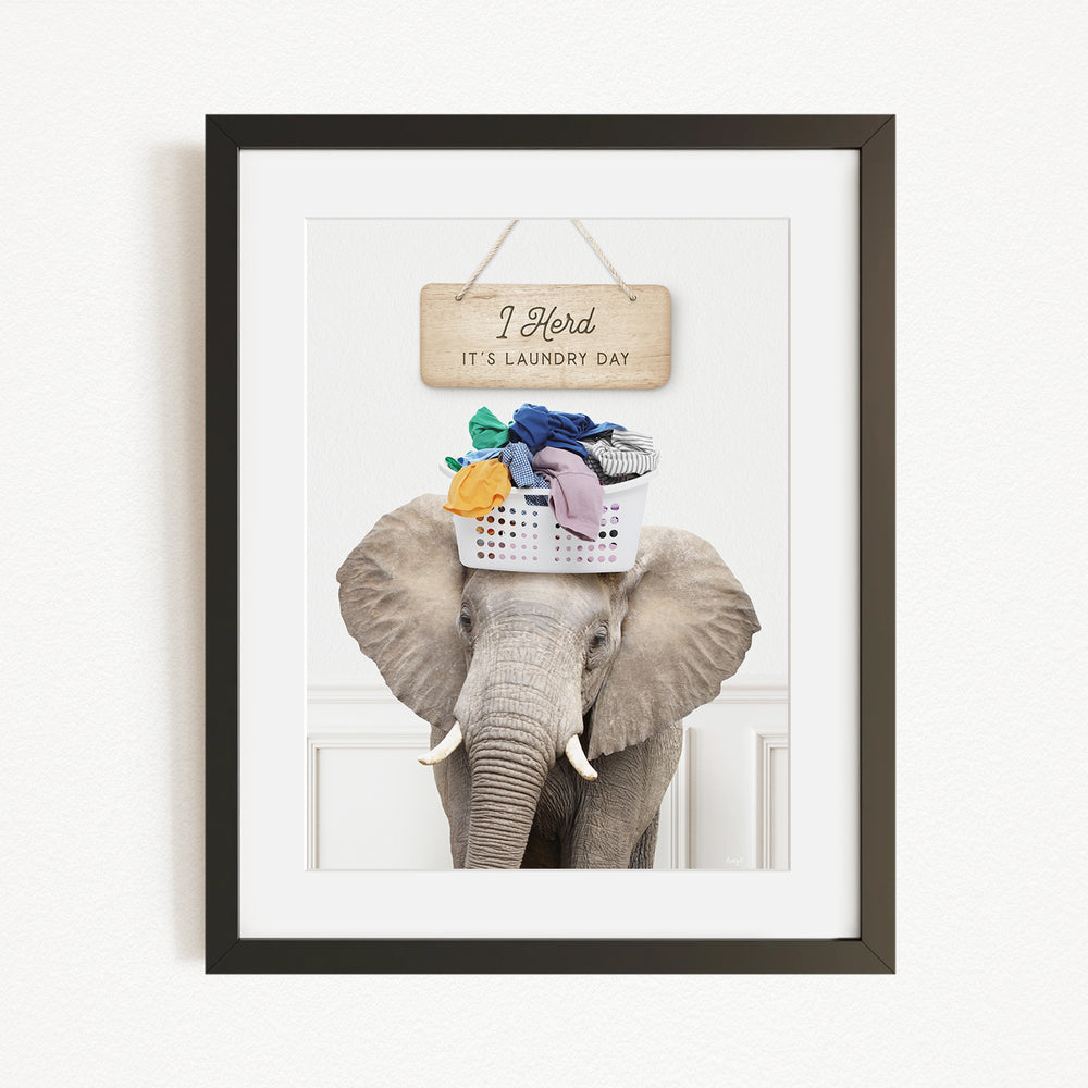 A framed image of an elephant carrying a basket of laundry on its head, with a sign above it that says "I Harded It's Laundry Day".