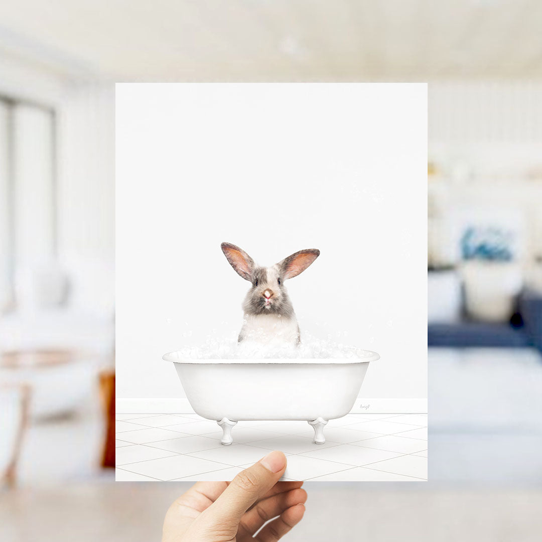 A hand holds up a framed image of a rabbit sitting in a bathtub filled with water.