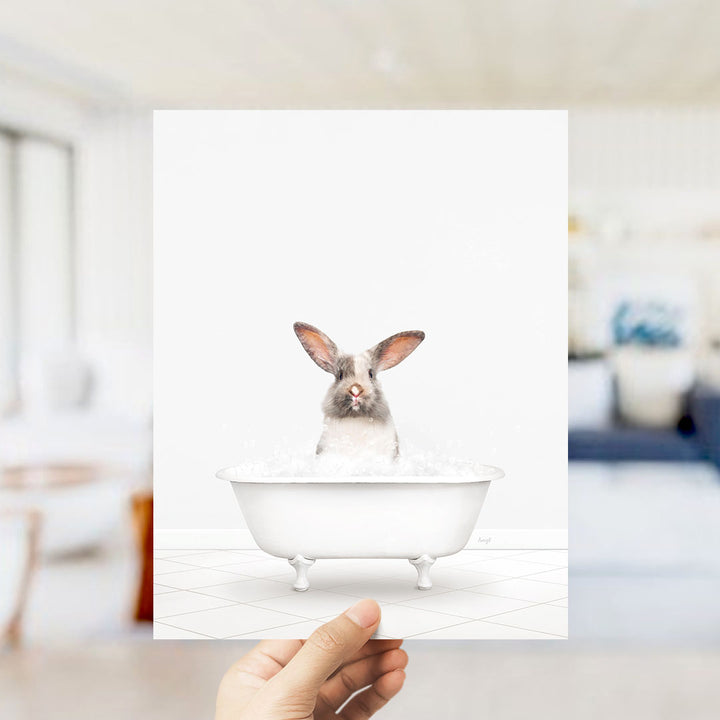 A hand holds up a framed image of a rabbit sitting in a bathtub filled with water.