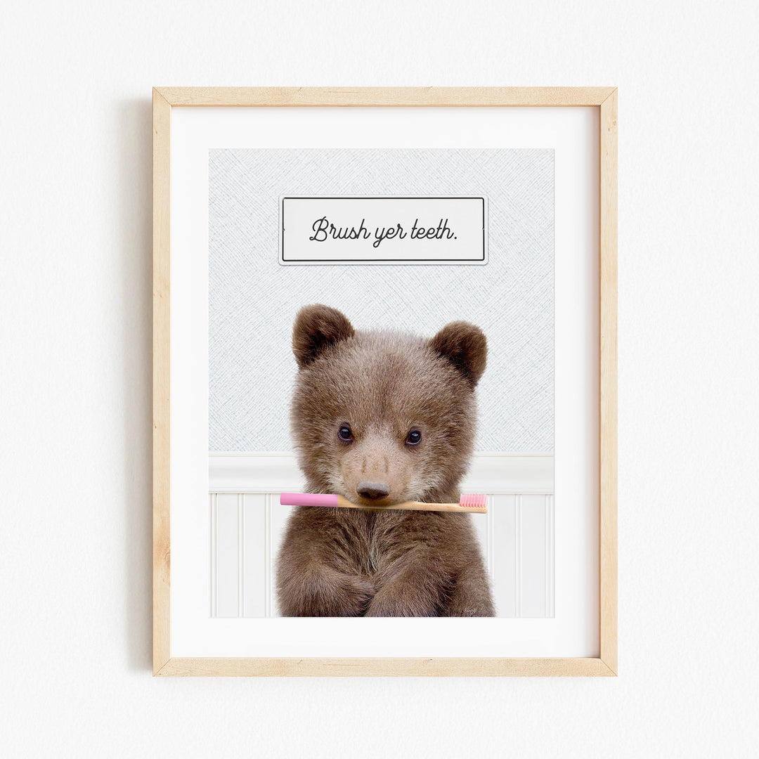 A cute brown bear holding a pink toothbrush in its mouth, with the text "Brush yer teeth" above it.
