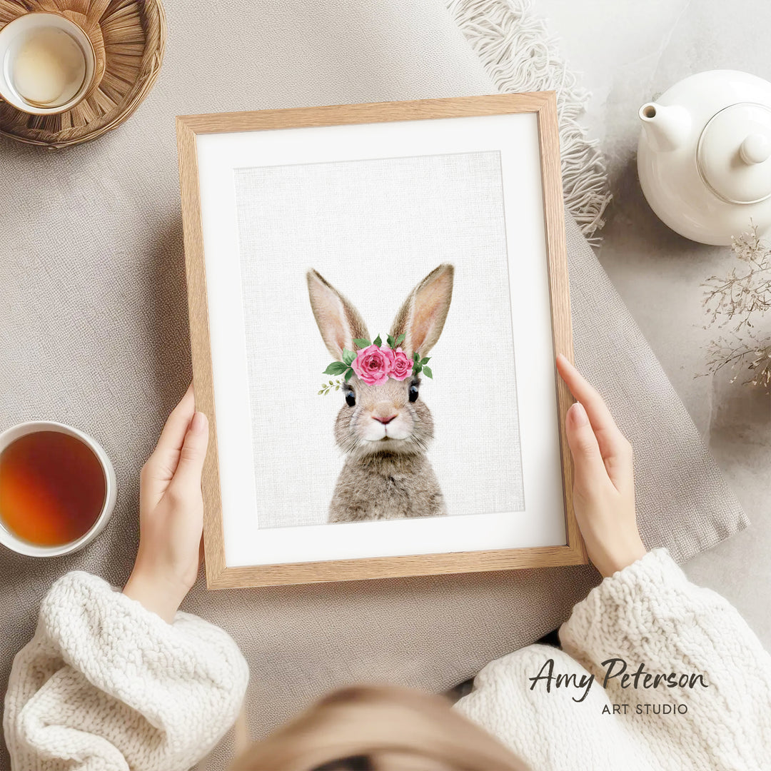 A person is holding a framed picture of a rabbit with a flower in its ear, surrounded by various objects such as a teapot, a cup, and a bowl.