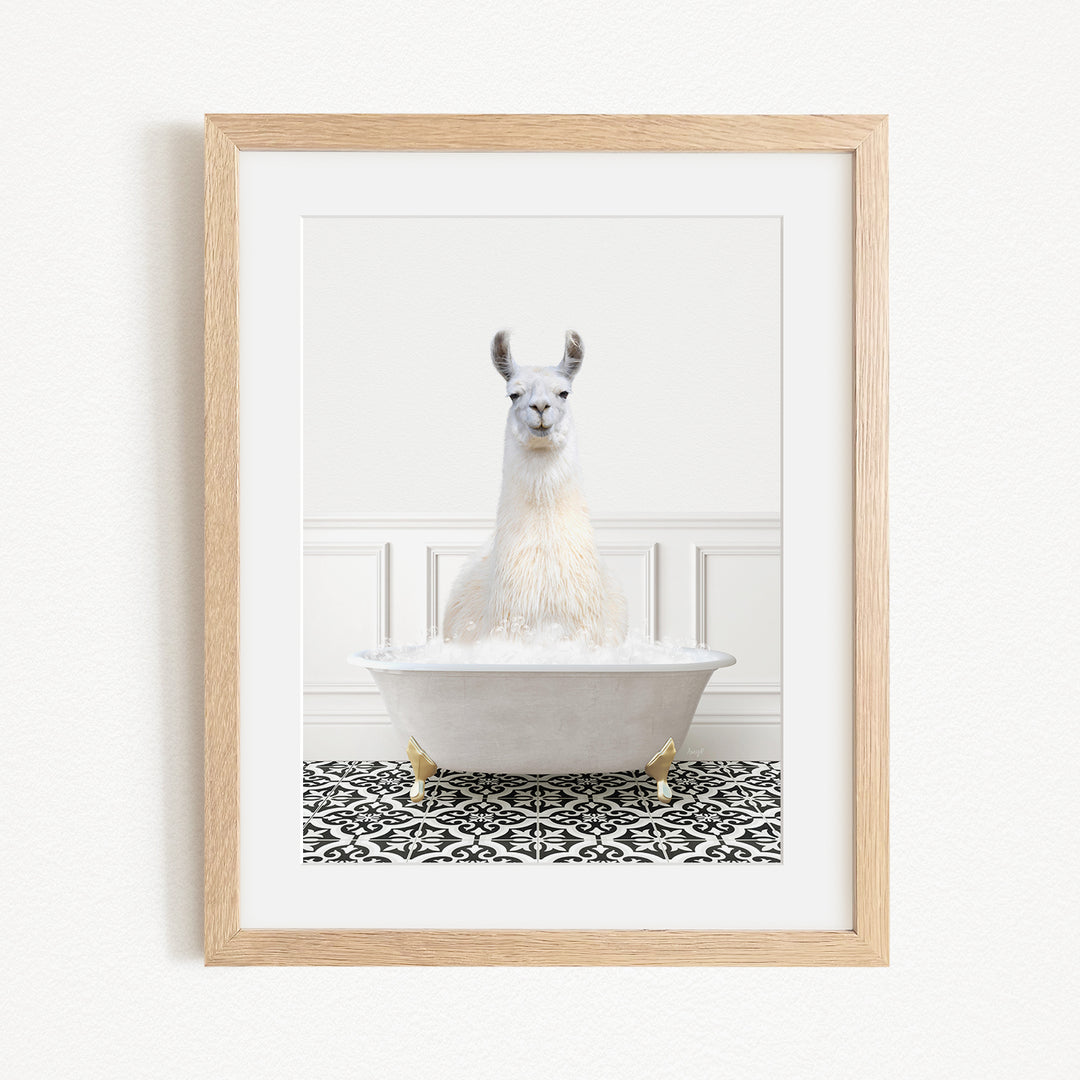A white llama sitting in a white bathtub filled with bubbles, with a black and white patterned rug on the floor beneath it.