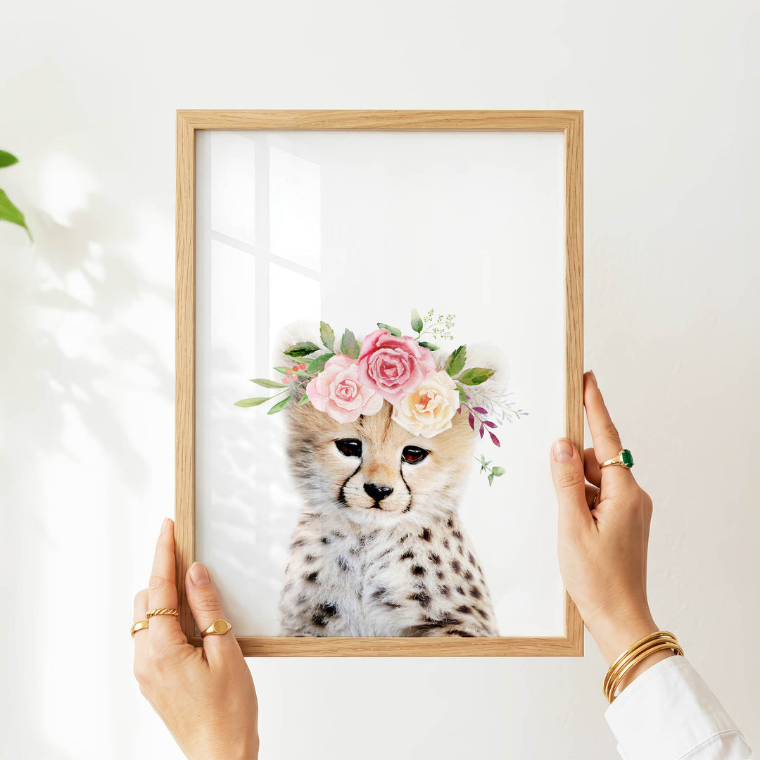 A person's hands are holding a framed picture of a cheetah wearing a floral crown.
