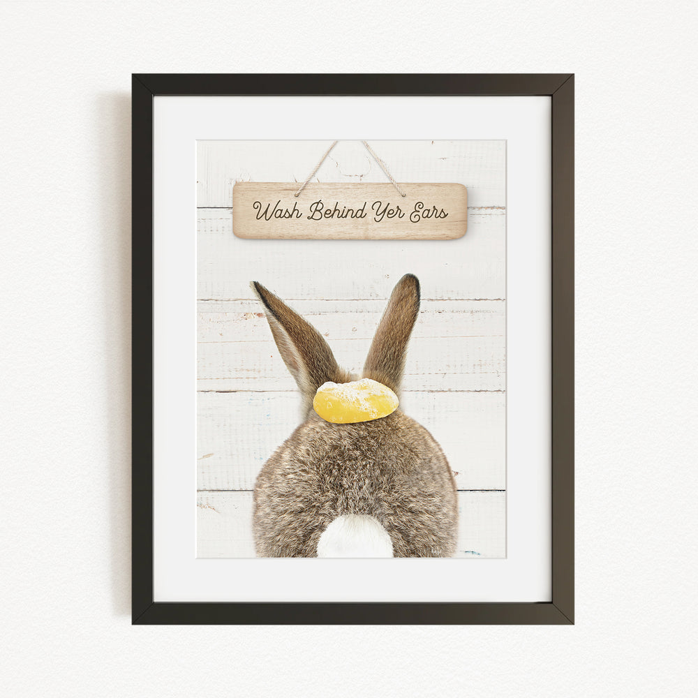 A framed image of a rabbit with a sign that says "Wash Behind Your Ears" hanging above it.