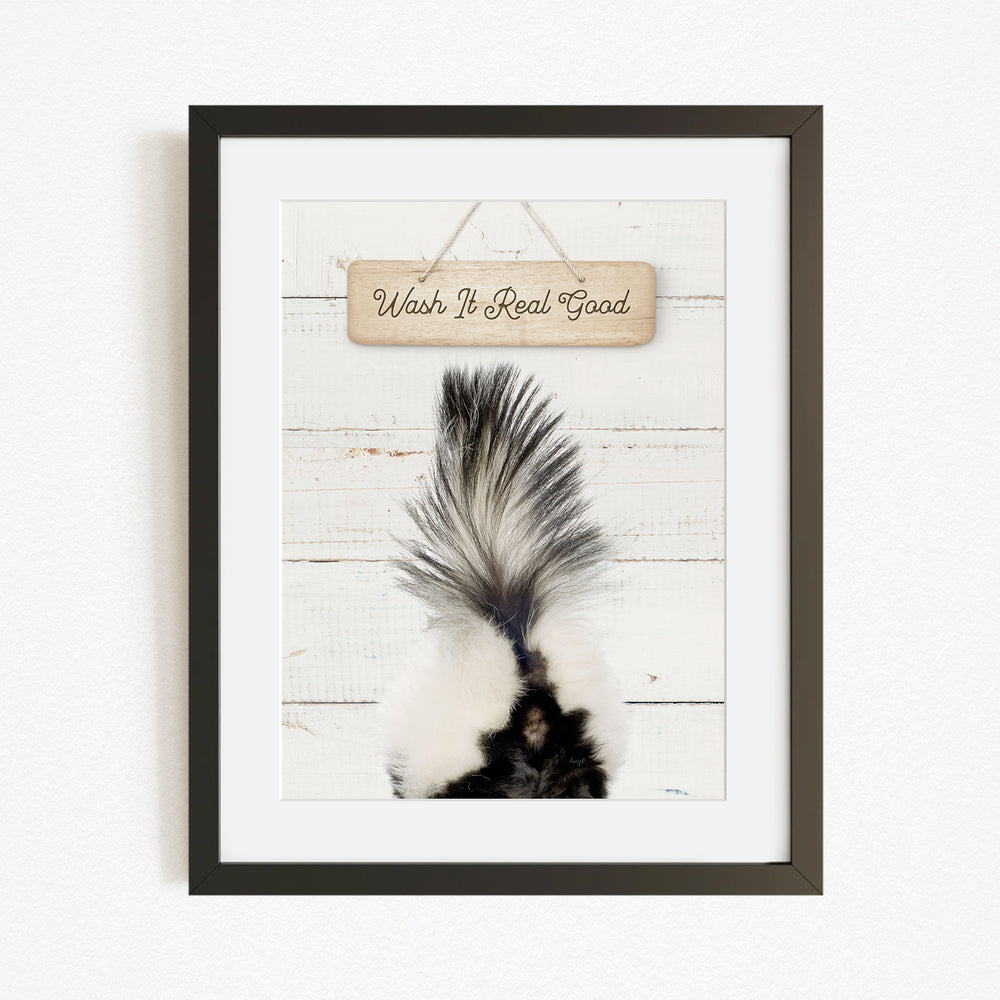 A framed image of a skunk's tail against a white wooden background, with a wooden sign above it that says "Wish It Real Good".
