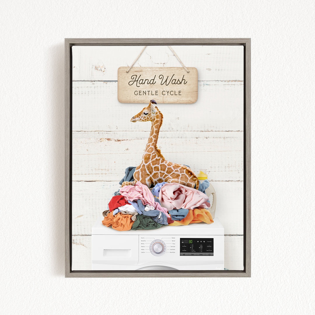 A giraffe sitting atop a pile of laundry, with a sign above that reads "Hand Wash Gentle Cycle".