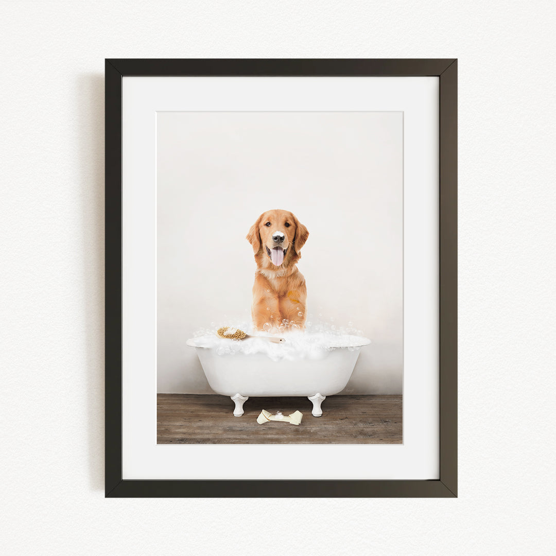 A golden retriever dog sitting in a white bathtub filled with bubbles, with a bone on the floor.