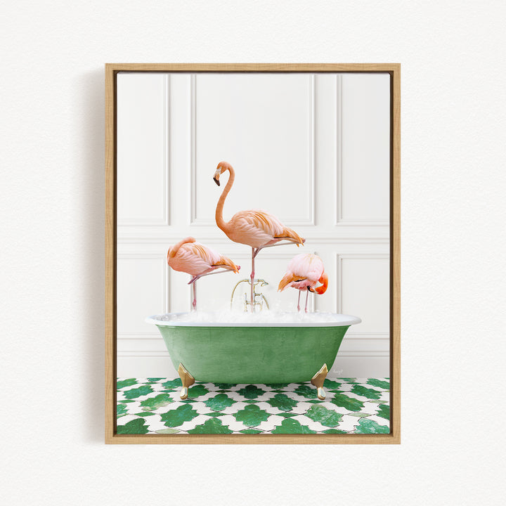 A framed image depicting three pink flamingos standing in a green bathtub filled with water, set against a white wall with a green and white patterned floor.
