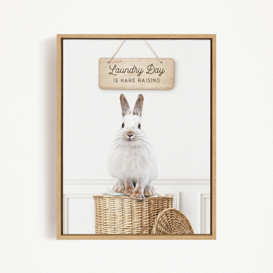 A white rabbit sitting on a woven basket, with a wooden sign above that says "Laundry Day is Hard Raising".