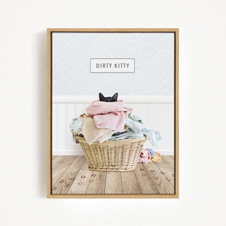A framed image depicting a cat sitting in a basket filled with laundry, with a sign above the basket that says "Dirty Kitty".