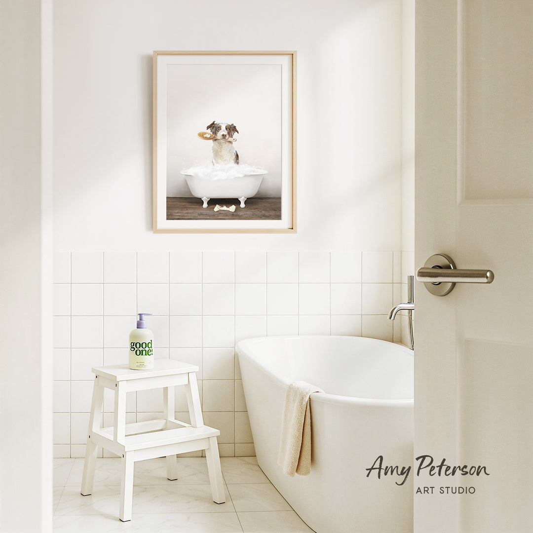A framed image of a dog sitting in a bathtub is displayed on the wall above a white bathtub in a clean, minimalist bathroom.