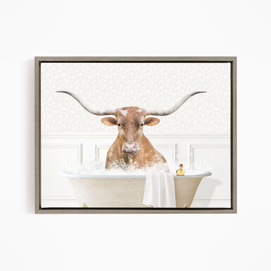 A bull with large horns is sitting in a bathtub filled with bubbles, with a towel and a small yellow object nearby.