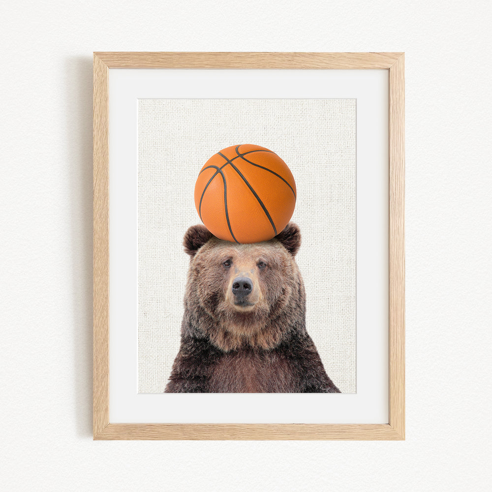 A brown bear sits on a basketball, creating a playful and whimsical scene.