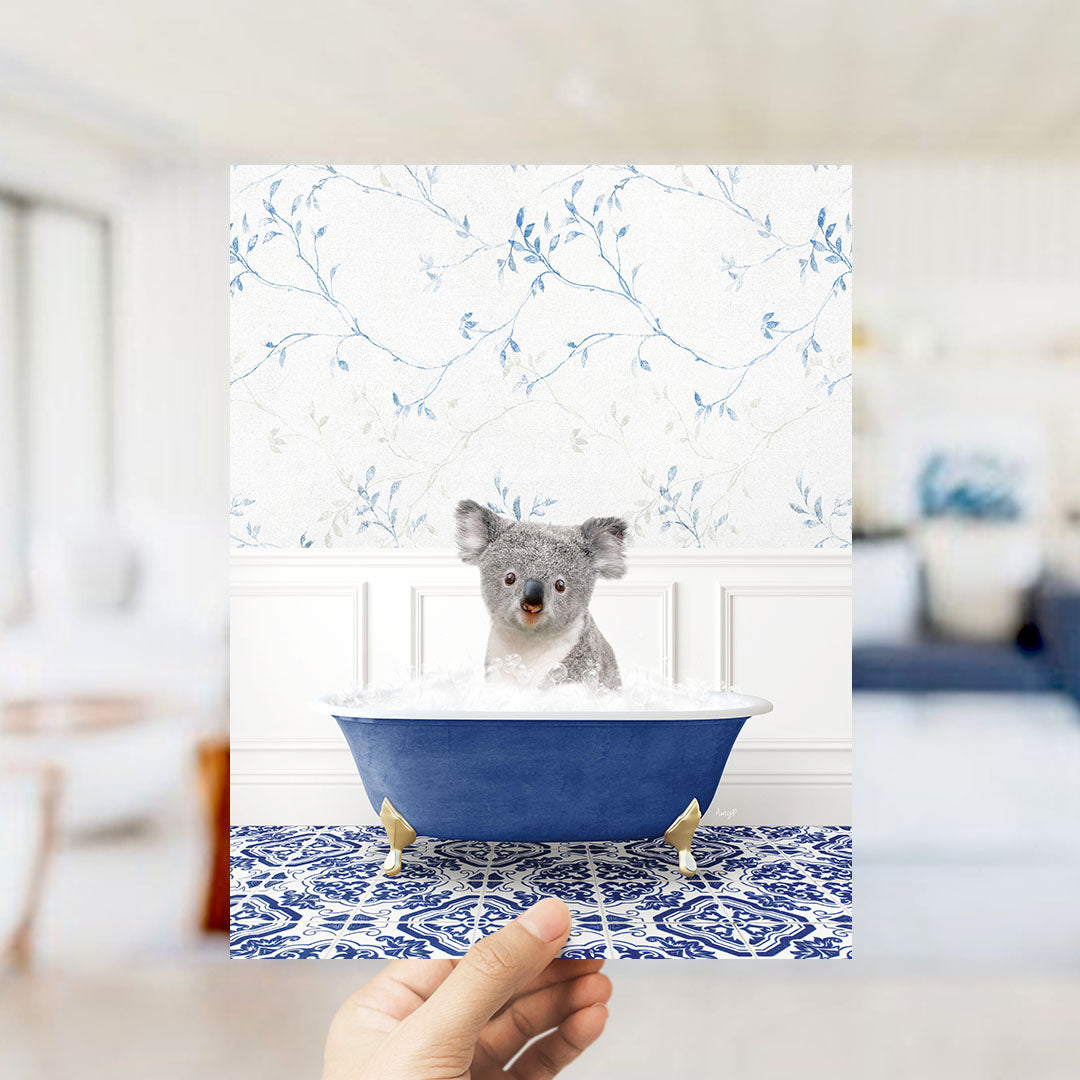 A koala bear sitting in a blue bathtub filled with bubbles, surrounded by a blue and white floral patterned wall.