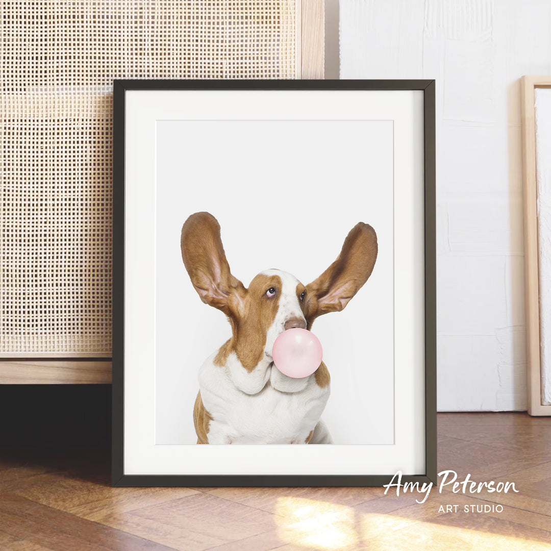 A framed photograph of a dog blowing a bubble gum bubble, with the dog's face and ears prominently featured in the center of the frame.