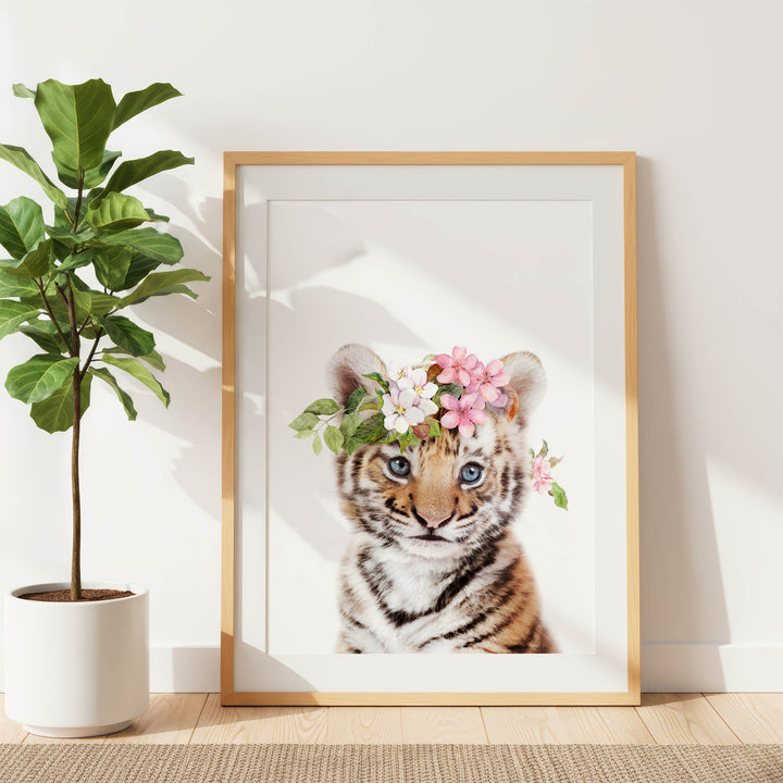 A framed photograph of a tiger cub wearing a flower crown, with a potted plant to the left.