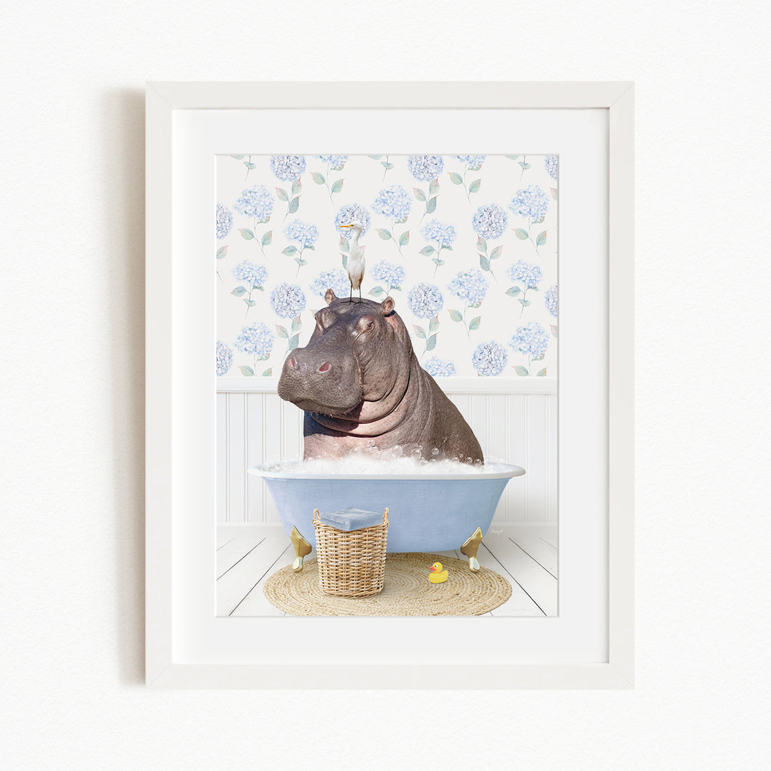 A framed image depicting a hippopotamus sitting in a bathtub filled with bubbles, surrounded by a blue floral patterned wall and a basket of rubber ducks.