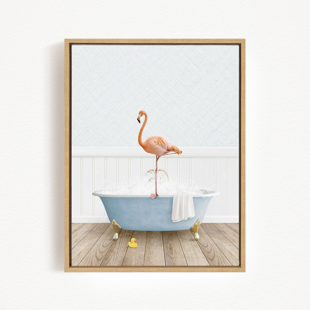 A framed image depicting a pink flamingo standing on a blue bathtub filled with water, with a towel and rubber duckies nearby.