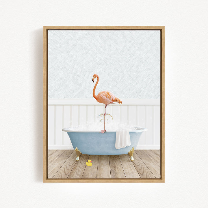 A framed image depicting a pink flamingo standing on a blue bathtub filled with water, with a towel and rubber duckies nearby.