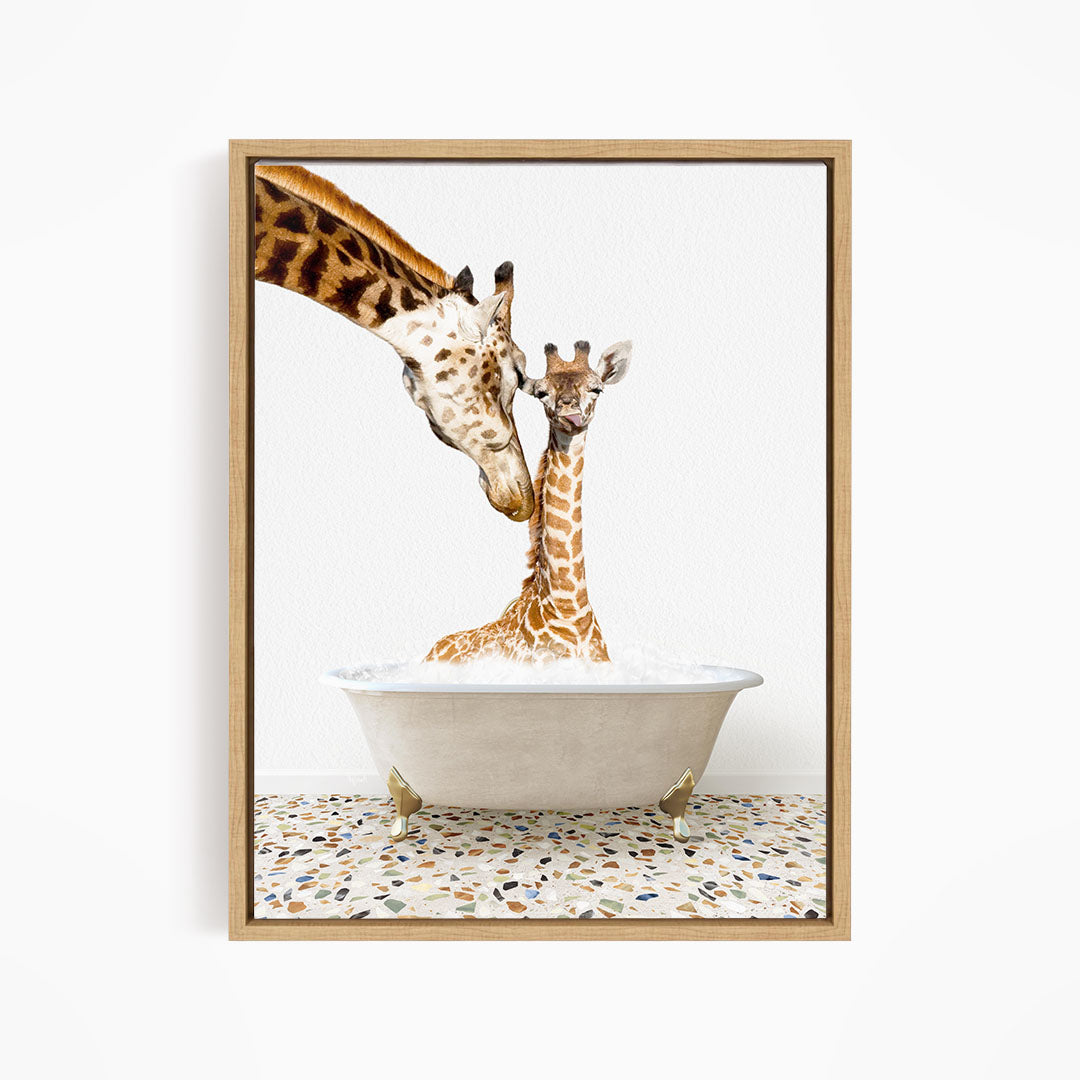 A mother giraffe and her baby giraffe are sitting together in a white bathtub, with the mother gently licking her baby.